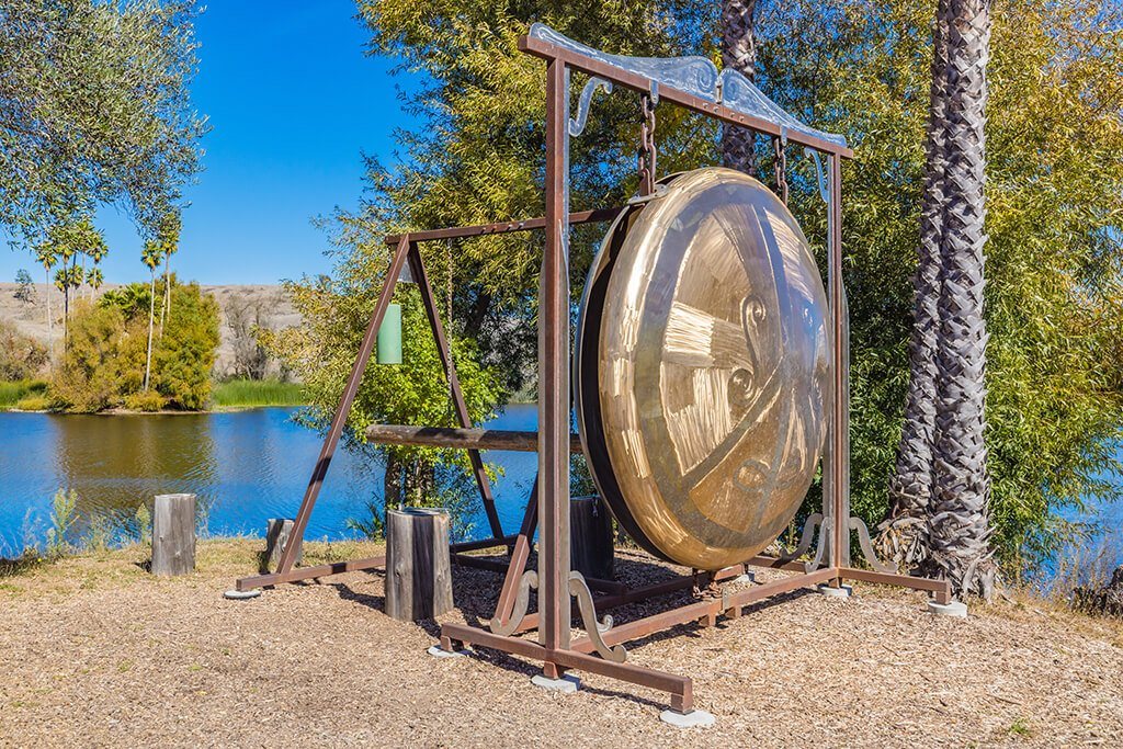 A large gong sits on a stand by a body of water